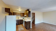 This two-story home offers a practical and comfortable layout designed for everyday living. The main floor showcases an open kitchen and living area connected by warm hardwood-style flooring that adds a cohesive, inviting feel throughout. The kitchen is well-appointed with dark wood cabinetry that provides ample storage, white appliances including a refrigerator and electric range, a double basin sink, and light-toned countertops that contrast nicely with the rich cabinetry. An L-shaped counter configuration maximizes workspace efficiency. A textured popcorn ceiling and flush-mount lighting keep the kitchen bright and functional. Adjacent to the kitchen, the living space opens up generously, offering room for comfortable furnishings. A staircase is visible from the main floor, leading to the second level of the home where additional living space is found. Neutral wall tones throughout the main level create a clean, versatile backdrop that complements a variety of décor styles. The overall design prioritizes functionality, with a straightforward floor plan that makes excellent use of the available space across both floors, making it a solid and practical place to call home.