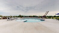Located at 700 S Main St in Oshkosh, Wisconsin, the Mill on Main outdoor amenity area offers a well-appointed, resort-inspired experience. The centerpiece of this space is a generously sized swimming pool with a classic curved design, complemented by a separate spa for relaxation. The pool deck is finished in clean, light-colored concrete and lined with lounge chairs, providing ample space for sunbathing and leisure.

Surrounding the pool area, the expansive patio is outfitted with multiple outdoor dining sets sheltered by large navy blue umbrellas, along with dedicated grilling stations ideal for outdoor entertaining. String lights are strung throughout, adding a warm, inviting ambiance for evening gatherings.

The space is enclosed by a sleek black iron fence that maintains an open feel while offering a clear sightline to the scenic waterfront and surrounding greenery beyond. The adjacent clubhouse building, constructed with brick and featuring tall glass windows, provides an architectural anchor to the outdoor space.

The multi-story residential building rises prominently in the background, its modern brick and neutral-toned facade offering a contemporary aesthetic. Together, the architectural elements and thoughtfully arranged outdoor furnishings create a vibrant, community-focused environment designed for year-round enjoyment.