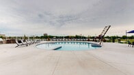 Located at 700 S Main St in Oshkosh, Wisconsin, the Mill on Main outdoor amenity area offers a well-appointed, resort-inspired experience. The centerpiece of this space is a generously sized swimming pool with a classic curved design, complemented by a separate spa for relaxation. The pool deck is finished in clean, light-colored concrete and lined with lounge chairs, providing ample space for sunbathing and leisure.

Surrounding the pool area, the expansive patio is outfitted with multiple outdoor dining sets sheltered by large navy blue umbrellas, along with dedicated grilling stations ideal for outdoor entertaining. String lights are strung throughout, adding a warm, inviting ambiance for evening gatherings.

The space is enclosed by a sleek black iron fence that maintains an open feel while offering a clear sightline to the scenic waterfront and surrounding greenery beyond. The adjacent clubhouse building, constructed with brick and featuring tall glass windows, provides an architectural anchor to the outdoor space.

The multi-story residential building rises prominently in the background, its modern brick and neutral-toned facade offering a contemporary aesthetic. Together, the architectural elements and thoughtfully arranged outdoor furnishings create a vibrant, community-focused environment designed for year-round enjoyment.