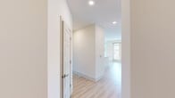 This single-floor residence showcases a clean, contemporary design with a neutral color palette of crisp whites and warm beige tones throughout. Light wood-look flooring runs continuously across the main living areas and bedrooms, creating a cohesive and airy feel.

The open-concept kitchen and living area serves as the heart of the space. The kitchen is equipped with stainless steel appliances, including a range, microwave, and refrigerator, complemented by taupe shaker-style cabinetry with gold hardware. A large central island with a white quartz countertop and a gold-finished faucet anchors the space, illuminated by a trio of globe pendant lights in a warm brass finish. The living area benefits from generous natural light through large windows and includes a ceiling fan.

A hallway connects the living spaces to the private areas, which include bedrooms with walk-in closets featuring built-in shelving. Two bathrooms feature large-format tile flooring, wood-toned vanity cabinetry with white countertops, and framed mirrors. The primary bathroom includes a glass-enclosed shower and access to a walk-in closet. Recessed lighting throughout ensures consistent, functional illumination across all rooms.