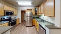 Located at 1435 Hampshire Ave S in St. Louis Park, Minnesota, this single-floor residence offers a functional and comfortable layout. The kitchen is a standout feature, equipped with stainless steel appliances including a refrigerator, electric range, microwave, and dishwasher. Light wood cabinetry provides ample storage, complemented by granite-style countertops, a double-basin sink, a decorative wine rack, and wood-look flooring that adds warmth throughout the cooking space. A peninsula counter connects the kitchen to the adjacent living and dining area, which transitions to plush carpeting and is fitted with a ceiling fan. A sliding glass door leads to a private balcony with views of surrounding greenery, and a wall-mounted air conditioning unit ensures year-round comfort alongside baseboard heating. The bedrooms are carpeted and offer generous proportions, with one featuring a spacious walk-in closet equipped with wire shelving and hanging rods. The bathrooms are clean and practical — one includes a wide vanity with a large mirror and shower, while the second features a soaking tub, tiled surround, and a wood-framed window that invites natural light and outdoor views. Textured ceilings are consistent throughout the home.