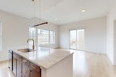 Located in Denver's vibrant Capitol Hill neighborhood, this thoughtfully designed 2-bedroom, 2-bathroom residence offers a seamless blend of modern aesthetics and functional living. Light wood flooring flows throughout, anchoring the clean, neutral palette found in every room. The open-concept kitchen and living area serves as the heart of the home, featuring rich dark wood cabinetry with brushed gold hardware, a striking marble-look quartz countertop island, a gas range, stainless steel appliances, and a marble-style backsplash. Large windows and a sliding glass door flood the space with natural light and frame sweeping city views of the Denver skyline, with direct access to a private balcony. Both bedrooms are generously proportioned, bright, and airy, each with access to outdoor balconies and ample natural light. The primary bedroom features a stylish sliding barn door leading to a dedicated closet. The two bathrooms are appointed with dramatic herringbone-patterned tile in deep metallic tones, brass and matte black fixtures, a soaking tub, and a glass-enclosed walk-in shower with a rain showerhead. A clean, well-lit hallway connects the private quarters to the main living spaces, completing this refined and contemporary urban residence.