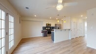 This well-appointed single-floor unit offers a thoughtfully designed open-concept layout that seamlessly connects the kitchen and living areas. Light wood-tone flooring flows throughout, creating a cohesive and inviting atmosphere.

The kitchen is a standout feature, showcasing a two-tone design with crisp white upper cabinetry and dark lower cabinets complemented by light quartz countertops. A dark tile backsplash adds visual contrast, while stainless steel appliances — including a gas range, over-the-range microwave, and French door refrigerator — provide a modern, functional cooking space. A peninsula with bar seating and pendant lighting serves as a natural divider between the kitchen and the open living area. A ceiling fan overhead adds comfort to the main living space.

The living area is bright and airy, featuring recessed lighting, a ceiling fan, and French doors flanked by windows that invite natural light and provide access to an outdoor space with views of surrounding greenery.

The bedroom is generously sized with a large window offering natural light and tree-lined views, complemented by light wood flooring and a ceiling fan. The bathroom features a glass-enclosed shower, wood-look tile flooring, and clean, neutral finishes throughout. Additional spaces include a hallway connecting the rooms, providing practical flow throughout the unit.