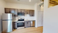 Located at 1301 Mulberry St in Des Moines, Iowa, this thoughtfully designed one-bedroom, one-bathroom unit makes excellent use of its compact footprint. The open-concept kitchen and living area serves as the heart of the space, showcasing rich dark-stained cabinetry, light quartz countertops, and a full suite of stainless steel appliances including a refrigerator, electric range, built-in microwave, and dishwasher. Light hardwood-style flooring runs throughout, brightening the interior and creating a cohesive, modern aesthetic. A tall, narrow window in the living area frames views of the surrounding Des Moines neighborhood, flooding the space with natural light. An eye-catching design detail is the exposed spiral ductwork that runs along the ceiling, lending an urban, industrial character to the otherwise clean and contemporary interior. The bedroom is a cozy, well-defined retreat featuring a ceiling fan and an open pass-through detail that connects it visually to the main living area. The combined bathroom and laundry room is efficiently arranged, offering a dark-cabinet vanity with a white sink, a full toilet, and a stacked washer and dryer unit — maximizing functionality without sacrificing comfort. A closet and hallway complete the well-organized layout of this modern urban residence.