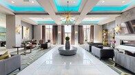 Located at 3800 SW Richsmith Rd in Bentonville, AR, this sophisticated single-floor amenity center offers an impressive collection of thoughtfully designed spaces spanning a generously sized footprint. The grand lobby sets a striking first impression with gleaming white marble-style tile floors, coffered ceilings accented by vibrant teal ambient lighting, and a dramatic sputnik chandelier. Curated seating areas are arranged around a central pedestal, while large windows dressed in floor-length drapes bathe the space in natural light. A linear fireplace flanked by decorative shelving and wall sconces anchors a refined lounge area with hexagonal-patterned carpeting and contemporary furnishings. The game room features billiard and shuffleboard tables beneath a teal-painted tray ceiling with chandelier lighting, complemented by gallery-style artwork throughout. A glass-enclosed wine bar showcases a floor-to-ceiling bottle display with a rolling library ladder, paired with a stylish poker room boasting herringbone wood flooring, shiplap walls, and a crystal chandelier. A private cinema delivers a classic theater experience with rows of bold red upholstered seats and projection screening. Rounding out the space is a conference room with a live-edge wood table, large windows overlooking lush greenery, and an artistic pendant light fixture.