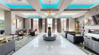 Located at 3800 SW Richsmith Rd in Bentonville, AR, this sophisticated single-floor amenity center offers an impressive collection of thoughtfully designed spaces spanning a generously sized footprint. The grand lobby sets a striking first impression with gleaming white marble-style tile floors, coffered ceilings accented by vibrant teal ambient lighting, and a dramatic sputnik chandelier. Curated seating areas are arranged around a central pedestal, while large windows dressed in floor-length drapes bathe the space in natural light. A linear fireplace flanked by decorative shelving and wall sconces anchors a refined lounge area with hexagonal-patterned carpeting and contemporary furnishings. The game room features billiard and shuffleboard tables beneath a teal-painted tray ceiling with chandelier lighting, complemented by gallery-style artwork throughout. A glass-enclosed wine bar showcases a floor-to-ceiling bottle display with a rolling library ladder, paired with a stylish poker room boasting herringbone wood flooring, shiplap walls, and a crystal chandelier. A private cinema delivers a classic theater experience with rows of bold red upholstered seats and projection screening. Rounding out the space is a conference room with a live-edge wood table, large windows overlooking lush greenery, and an artistic pendant light fixture.