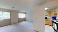 This single-floor unit presents a clean, functional layout finished throughout in neutral tones that create a bright and cohesive atmosphere. The living area is generously proportioned, featuring plush wall-to-wall carpeting and multiple windows dressed with vertical blinds that allow natural light to filter into the space. The open feel is enhanced by smooth white ceilings and a ceiling fan, providing both comfort and ventilation.

The kitchen is equipped with warm honey-toned wood cabinetry offering ample upper and lower storage, laminate countertops, a stainless steel sink, a gas range with overhead ventilation, and a dishwasher. White tile backsplash lines the walls, adding a clean, classic finish to the functional cooking space.

The bathroom features a wide vanity with a white countertop, an undermount sink, wood cabinetry below, and a large wall-spanning mirror with overhead globe lighting. A decorative framed mirror adds visual interest, while the layout offers a practical and organized feel.

Additional rooms include well-sized carpeted bedrooms with neutral walls providing a versatile canvas, along with closet access visible from connecting hallways. Throughout, the space maintains a simple, understated design suited to a variety of living arrangements.