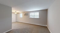 This efficiently designed 2-bedroom, 1-bathroom unit offers a practical and comfortable layout across a single floor. The spacious primary bedroom is carpeted in neutral tones and features a large wall-to-wall closet with bi-fold doors, a baseboard heating unit, and a window offering views of surrounding greenery. The second bedroom is similarly finished with carpet flooring, neutral gray walls, baseboard heating, and a window that brings in natural light. The living area is generously proportioned, with carpet flooring, neutral beige walls, a ceiling fan, and two windows fitted with blinds, along with a wall-mounted air conditioning unit for added comfort. The kitchen is well-equipped, showcasing rich cherry wood cabinetry, granite-style countertops, a tile backsplash, and light tile flooring. It includes a full-size refrigerator, a gas range, and a dishwasher. The bathroom features a full soaking tub with chrome fixtures, complemented by marble-look ceramic tile surround walls and crisp white fixtures throughout. Baseboard heating is present throughout the unit, ensuring consistent warmth, while multiple windows provide pleasant natural light and outdoor views across all rooms.