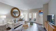 Located at 3301 Glenn McConnell Pkwy in Charleston, SC, this single-floor residence offers a thoughtfully designed open-concept layout that balances comfort and functionality. The living room serves as the heart of the home, featuring rich hardwood-style flooring, neutral toned walls, and a set of elegant French doors that flood the space with natural light and provide direct access to an outdoor area. The kitchen is well-appointed with white cabinetry, granite-style countertops, stainless steel appliances, and a peninsula with pendant lighting that seamlessly connects to a dedicated dining area. The bedrooms are generously sized, each featuring plush carpeting, large windows that invite natural light, and ceiling fans for comfort. The bathroom is clean and modern, outfitted with tile flooring, a sleek sliding glass shower enclosure, and an extended vanity with ample storage. A dedicated laundry room with wire shelving and washer/dryer hookups adds everyday convenience, while an additional utility/storage area with built-in shelving provides practical organization. Throughout the residence, a cohesive coastal-inspired color palette and consistent finishes create a bright, welcoming ambiance reflective of Charleston's relaxed yet refined lifestyle.