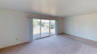 This single-floor residence offers two bedrooms and one and a half bathrooms across a well-organized and functional layout spanning just over 1,000 square feet. The living area is a standout space, featuring large sliding glass doors that open to a private balcony overlooking lush greenery and mature trees, flooding the room with natural light and providing pleasant outdoor views. The neutral-toned carpet and clean white walls create a bright, open atmosphere throughout the living spaces.

The galley-style kitchen is efficiently designed with white cabinetry lining both sides, offering ample storage and counter space. A stainless steel sink, white appliances including a full-size refrigerator, and warm hardwood-style flooring complete the kitchen's practical and tidy aesthetic.

Both bedrooms are carpeted and feature windows with blinds that allow for natural light while maintaining privacy. Each room provides a comfortable, versatile space suitable for a variety of furniture arrangements. Closet storage is available, including a paneled bifold closet door visible in one of the rooms.

The bathroom areas are cleanly finished with tile flooring, a wall-mounted medicine cabinet with mirror, and a countertop vanity. A carpeted hallway connects the bedrooms and bathrooms, contributing to the cohesive flow of the residence. Overall, the space presents a clean, move-in ready environment with a neutral palette throughout.
