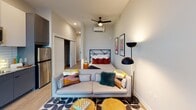 Located at 614 Rigsbee Ave in Durham, NC, this single-floor studio unit showcases a thoughtfully designed open-concept layout with modern finishes throughout. Light wood-style flooring flows continuously across the space, complementing the clean, neutral color palette that defines the interior.

The combined living and sleeping area is efficiently arranged, featuring a ceiling fan, a wall-mounted mini-split system for climate control, and a dedicated closet. Large windows flood the space with natural light while offering expansive views of the surrounding Durham cityscape and beyond.

The kitchen is outfitted with two-tone cabinetry—matte gray lower cabinets paired with white upper cabinets—granite countertops, a white subway tile backsplash, and stainless steel appliances including a dishwasher, microwave, and refrigerator. A corner window in the kitchen further enhances natural light and city views.

The bathroom is neatly appointed with a dark gray vanity featuring a granite countertop, wood-tone flooring, and clean white walls accented with matte black hardware. The overall ambiance of the unit is contemporary and polished, reflecting the modern urban character of downtown Durham.