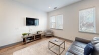 Located at Brooklyn Village in uptown Charlotte, NC, this one-bedroom, one-bathroom unit offers a thoughtfully designed layout that maximizes every square foot. The open-concept kitchen and living area serves as the heart of the home, featuring a fully equipped kitchen with stainless steel appliances—including a refrigerator, electric range, built-in microwave, and dishwasher—complemented by gray shaker-style cabinetry that extends to the ceiling, a classic white subway tile backsplash, and a built-in wine rack. Natural light filters through windows fitted with blinds, brightening the living space which accommodates a comfortable seating area with a wall-mounted flat-screen TV and warm wood-look flooring that flows throughout the unit. A sliding barn-style door adds a contemporary touch to the entryway corridor. The bedroom is a calm retreat, complete with a ceiling fan, recessed lighting, a double-door closet with gray paneled doors, and direct access to the full bathroom. The bathroom features large-format tile flooring, a clean white vanity with ample cabinet storage, and a minimalist, bright aesthetic. The hallway connects all spaces efficiently, contributing to a cohesive and functional floor plan.