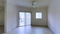 This single-floor residence offers a well-organized layout designed for comfortable everyday living. The floor plan reveals a series of interconnected rooms, including a living area, kitchen, bathroom, and additional private rooms, all arranged to maximize functionality and flow.

The living area serves as the heart of the home, featuring large-format light tile flooring that extends throughout the space, lending a clean and cohesive aesthetic. A ceiling fan with a light fixture anchors the room, providing both comfort and illumination. Natural light floods the interior through a full-width sliding glass door fitted with vertical blinds, which opens directly onto a covered balcony with outdoor views of surrounding greenery. A secondary window further brightens the space.

The kitchen is equipped with cabinetry and appliances arranged efficiently along the walls, offering ample storage and workspace. Adjacent areas provide additional utility and privacy, with the bathroom tucked neatly into the interior of the floor plan.

Throughout the home, the textured ceiling treatment adds architectural character, while the neutral color palette across walls and floors creates a bright, airy atmosphere. The overall layout is practical and well-proportioned, making this a comfortable and inviting single-floor living space.