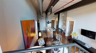 Located within the historic Germantown Mill Lofts, this single-floor loft unit showcases a striking blend of industrial character and modern living. The open-concept layout seamlessly connects the living, dining, and kitchen areas, creating a spacious and cohesive environment. Original timber ceiling beams and exposed ductwork run overhead, preserving the mill building's authentic industrial heritage. Dark hardwood floors anchor the space and complement the raw architectural details throughout.

The kitchen features a central island with bar seating, pendant lighting, and modern fixtures, making it both functional and visually prominent within the open floor plan. A dedicated dining area sits adjacent, offering a natural flow for entertaining. The living area provides ample room for furnishings, enhanced by the soaring ceiling height that amplifies the sense of openness.

Structural steel columns punctuate the space, reinforcing the industrial aesthetic, while neutral wall tones and carefully placed lighting add warmth. The overall ambiance balances the rugged character of a converted mill building with comfortable, contemporary livability.