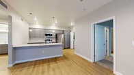 This single-floor residence offers a thoughtfully designed layout across three bedrooms and two bathrooms. The open-concept kitchen and living area serves as the heart of the home, anchored by a large central island with a granite-look countertop, undermount sink, and pendant lighting overhead. Gray shaker-style cabinetry lines the kitchen walls, complemented by stainless steel appliances including a refrigerator, range, and microwave. Light wood-look flooring extends throughout the main living areas, contributing to a clean, modern aesthetic.

The primary bedroom features a ceiling fan and sliding glass doors that invite natural light and outdoor access. Its en-suite bathroom is appointed with a wide granite vanity, gray cabinetry, a framed mirror, and a glass-enclosed shower. A dedicated walk-in closet with built-in shelving and hanging rods provides organized storage.

The additional bedrooms are carpeted and offer neutral wall tones, making them versatile spaces. The second bathroom mirrors the same granite vanity and gray cabinetry design. A dedicated in-unit laundry area with side-by-side washer and dryer hookups is conveniently accessible from the kitchen. Throughout, the home maintains a cohesive, contemporary palette with white trim and neutral walls.