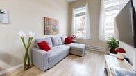 Located at 123 King St in the heart of London, Ontario, this efficient one-bedroom, one-bathroom unit offers a well-organized layout across a single floor. The open-concept living room and kitchen area forms the heart of the space, where light wood laminate flooring, warm neutral wall tones, and a large window with sheer curtains create a bright and welcoming atmosphere. A sectional sofa and a colorful wall painting add character to the living area, which benefits from views of the surrounding streetscape. The kitchen is efficiently designed with white cabinetry extending to the upper walls, a full suite of appliances including a stove, refrigerator, and microwave, as well as a double sink and a light countertop that extends into a small breakfast bar. Tile flooring grounds the kitchen area and provides a clean contrast to the rest of the unit. The bedroom is a cozy and well-lit retreat, featuring a window that frames outdoor views and provides ample natural light. Neutral walls keep the space calm and restful. The bathroom is clean and functional, finished with a full bathtub and shower enclosure, a toilet, and speckled tile flooring in soft neutral tones. Throughout the unit, the consistent use of light colors and natural light contributes to an airy and comfortable ambiance.