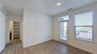 This single-floor unit presents a clean, modern aesthetic throughout, characterized by crisp white walls, recessed lighting, and consistent hardwood-style flooring that flows seamlessly from room to room. The main living area is open and well-proportioned, featuring a glass-paneled door that leads to a private balcony, allowing natural light to filter in while offering outdoor views. An adjacent window further enhances the brightness of the space.

The kitchen is thoughtfully designed with dark wood-grain cabinetry extending to the ceiling for ample storage, paired with light granite countertops and a white subway tile backsplash. Stainless steel appliances, including a refrigerator, range, microwave, and dishwasher, complete the functional layout.

The bedroom is a comfortable, well-lit room featuring two windows that frame outdoor views and a ceiling fan for added comfort. Its neutral tones and hardwood-style flooring maintain the unit's cohesive design language.

The bathroom is finished with dark cabinetry, granite countertops, a large mirror, and a tiled tub-shower combination featuring marble-style tile. The overall layout, as seen from the aerial floor plan view, is compact yet efficiently organized, making effective use of every available area.