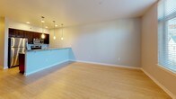 This single-floor space offers a clean, contemporary design with a cohesive aesthetic carried throughout. Light hardwood flooring runs across the main living and sleeping areas, lending warmth and visual continuity to the open layout. The living area is generously proportioned, with neutral-toned walls and a bright, airy feel that creates a versatile canvas for furnishing.

The galley-style kitchen is well-appointed, featuring dark espresso cabinetry paired with speckled granite countertops that extend to a peninsula counter overlooking the living area. Stainless steel appliances, including a refrigerator, range, and built-in microwave, are integrated seamlessly into the cabinetry. Pendant lighting fixtures hang above both the peninsula and the main kitchen workspace, providing focused illumination while adding a modern design touch. Recessed ceiling lights further enhance the kitchen's functionality.

The bathroom continues the granite countertop theme, with a dark vanity cabinet, an undermount sink, and a large wall mirror. A shower/tub combination and neutral tile work complete the space. A dedicated bedroom area with a closet alcove provides practical storage. Overall, the unit maintains a consistent, modern palette throughout.