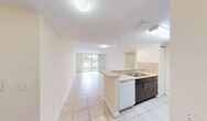 Located at 750 NW 8th St in Florida City, FL, this three-bedroom, two-bathroom single-floor residence offers a practical and well-organized layout. Light-toned ceramic tile flooring runs throughout the entire home, creating a clean, cohesive look. The open-concept kitchen and living area forms the heart of the space, where a peninsula with a built-in sink and light countertop provides both prep space and a natural divider. The kitchen features dark cabinetry contrasted by white appliances, including a range, microwave, refrigerator, and dishwasher, complemented by a beige tile backsplash. The living area extends toward a full-length sliding glass door that fills the space with natural light and opens to a view of lush tropical greenery. Each bedroom is equipped with a ceiling fan and window, with the primary bedroom offering a comfortable footprint. Both bathrooms are finished with matching beige tile surrounds in the tub-shower combinations, vanity mirrors, and neutral countertops, lending a consistent and clean aesthetic. A dedicated hallway connects the rooms efficiently, and a closet provides additional storage. The overall ambiance is bright, airy, and low-maintenance—well-suited for the warm South Florida climate.