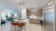 Located at 2410 Canopy Breeze Circle in Orlando, Florida, this single-floor residence offers a thoughtfully designed layout with modern finishes throughout. The open-concept kitchen serves as the heart of the home, showcasing flat-panel cabinetry in a warm wood tone, a herringbone-patterned tile backsplash, quartz countertops, stainless steel appliances, and a central island with bar seating — ideal for both cooking and casual dining. Light wood-look flooring flows seamlessly throughout the space, enhancing the bright, cohesive aesthetic. The living room is bathed in natural light through large windows and a glass door, creating an airy and welcoming atmosphere with ample room to relax. The bedrooms are generously sized, each featuring large windows with abundant natural light, ceiling fans, and a calm, neutral palette. The primary bathroom is well-appointed with a wood-toned double vanity, a walk-in glass-enclosed shower, and clean tile work. A secondary bathroom offers a full soaking tub with tiled surround and built-in open shelving for organized storage. Completing the home is a dedicated in-unit laundry room with a full-size washer and dryer, providing added convenience and functionality for everyday living.