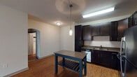 This single-floor, one-bedroom, one-bathroom unit offers a practical and modern layout designed to maximize comfort and functionality. The kitchen serves as a central highlight, featuring rich dark cabinetry that extends to the ceiling for ample storage, stainless steel appliances including a refrigerator, range, microwave, and dishwasher, and a double-basin sink. A pendant light fixture adds a stylish accent above the kitchen island area, complementing the overhead fluorescent lighting. Wood-look flooring runs throughout the kitchen and living areas, lending warmth and easy maintenance to the space.

The living area connects seamlessly to the kitchen through an open layout, with an arched doorway adding an architectural detail that softens the transition between spaces. The bedroom is carpeted for comfort and features a ceiling fan, a large window that allows natural light in and provides outdoor views, and a calm, neutral color palette that creates a relaxing atmosphere.

The bathroom includes a full soaking tub and shower combination finished with white subway tile and a decorative navy accent stripe. Brushed nickel grab bars and fixtures offer both style and practicality. Wood-look flooring continues into the bathroom, maintaining a cohesive aesthetic throughout the unit.
