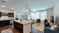 This single-floor residence is designed with an open-concept layout that seamlessly connects the kitchen, dining, and living areas into one cohesive, light-filled space. The kitchen is a standout feature, showcasing dark espresso cabinetry, granite countertops, a subway tile backsplash, and a full suite of stainless steel appliances. A large center island with seating provides additional workspace and serves as a natural gathering point. Pendant lighting above the island and recessed ceiling lights ensure ample illumination throughout.

The living area benefits from multiple large windows dressed with blinds and floor-length curtains, allowing generous natural light. A ceiling fan overhead adds both function and comfort. Rich hardwood-style flooring flows throughout the main living spaces, adding warmth and continuity to the design.

The two bedrooms are carpeted for comfort and each includes a ceiling fan and windows with natural light. The primary bedroom connects to a walk-in closet. The bathrooms feature matching dark cabinetry, granite vanity tops, and tile flooring, with one bathroom offering a full tub-shower combination. A dedicated in-unit laundry room with a full-size washer and dryer completes this well-equipped residence.
