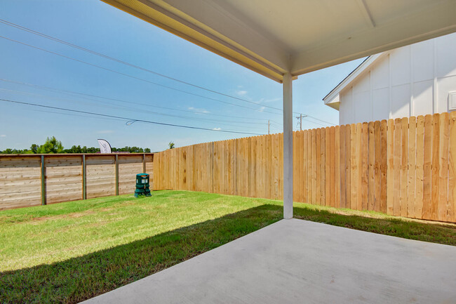 Patio trasero cubierto con losa de hormigón, valla de madera para mayor privacidad y jardín con césped. - Legacy Farms