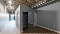Located at 20300 Civic Center Dr in Southfield, Michigan, this single-floor unit blends modern finishes with striking industrial design elements. The open layout is anchored by soaring exposed ceilings featuring raw structural trusses, spray foam insulation, and visible ductwork, creating an urban loft aesthetic throughout. Light wood-tone luxury vinyl plank flooring runs through the main living and kitchen areas, while darker hardwood-style flooring defines the sleeping area, adding visual contrast and depth.

The kitchen is efficiently designed with warm wood-toned cabinetry, stainless steel appliances including a range, microwave, dishwasher, and refrigerator, and open shelving that complements the industrial character of the space. The living area benefits from a large glass entry door that floods the unit with natural light and provides a direct view to the outdoors.

The sleeping area is well-organized, featuring a dedicated walk-in closet with a full rod system and a separate secondary closet with a sliding mirrored door. A private bathroom with a clean, modern door completes the layout. Cool gray walls throughout unify the space, balancing the warmth of the flooring and cabinetry for a cohesive, contemporary feel.