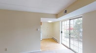 This single-floor unit offers a clean, functional layout with a warm, neutral color palette carried consistently throughout. The open living and dining area is generously proportioned, featuring light-toned wall-to-wall carpeting, cream-colored walls, and a textured ceiling. A large sliding glass door floods the space with natural light and provides views of the surrounding greenery, while a baseboard heating system ensures year-round comfort. The transition between the carpeted living area and the kitchen is marked by light hardwood-style flooring. The kitchen is well-equipped with warm wood cabinetry, ample counter space, a full suite of white appliances including a refrigerator and electric range, and a stainless steel sink — all complemented by a practical overhead ventilation hood. Two carpeted bedrooms each feature large windows that invite natural light and offer outdoor views, along with individual baseboard heaters. The full bathroom is neatly appointed with warm wood vanity cabinetry, a light countertop, hardwood-style flooring, and a separate water closet for added privacy. Throughout the unit, the consistent use of soft neutral tones and practical finishes creates a cohesive and inviting atmosphere.