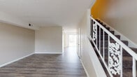 This two-story residence offers a practical and well-organized layout across both levels. The main floor greets visitors with a spacious open living area finished in durable wood-style flooring in a warm grey-brown tone, complemented by neutral beige walls and a textured ceiling. A staircase with a distinctive white decorative railing and a bold yellow accent wall serves as a visual focal point, connecting the two floors. Natural light filters through a sliding glass door at the rear of the main level, brightening the open living and hallway areas. The kitchen is efficiently designed with white cabinetry, granite-look countertops, a double sink, and a built-in electric range with overhead ventilation. Upper-level bedrooms are generously sized, each featuring the same wood-style flooring, neutral walls, textured ceilings, and windows that bring in ample natural light. Ceiling fans are present in multiple bedrooms for added comfort. The bathrooms are clean and functional; one full bath includes a tub-shower combination, a vanity with matching granite-look countertops, and wood-look tile flooring, while a half bath provides additional convenience. Overall, the space presents a consistent, move-in-ready aesthetic throughout.