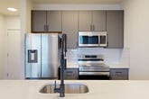Located at 4200 N Carlin Springs Rd in Arlington, Virginia, this efficiently designed unit offers a well-considered layout that maximizes every square foot across a single floor. Light-toned hardwood-style flooring runs throughout the living areas, complementing the clean white walls and creating a bright, cohesive aesthetic. Large windows dressed with horizontal blinds allow generous natural light to fill the space while framing views of the surrounding Arlington urban landscape.

The modern kitchen serves as a functional centerpiece, featuring sleek gray flat-front cabinetry, a white subway tile backsplash, and a full suite of stainless steel appliances including a French door refrigerator, electric range, and over-the-range microwave. A peninsula with a crisp white quartz countertop and an integrated sink with a matte black spring-neck faucet provides additional prep space and a natural transition into the living area, accented by stylish pendant lighting overhead.

The bathroom is finished with large-format light tile, a soaking tub with shower, and matte black fixtures that add a contemporary touch. A dedicated in-unit laundry closet houses a stacked washer and dryer for added convenience. Two closets provide practical storage, while a ceiling fan with light in the main living area enhances comfort year-round.