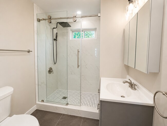 Baño totalmente renovado con azulejos de ducha con apariencia de mármol, puerta de ducha de vidrio y tocador moderno. - 78 Orchard St