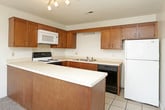 This single-floor unit offers a practical and straightforward layout, as illustrated by the floorplan. The kitchen is equipped with warm-toned wooden cabinetry, light countertops, and a full suite of appliances, including an electric range, built-in microwave, dishwasher, and refrigerator. A peninsula separates the kitchen from the adjacent living area, which transitions from tile flooring to plush carpet. The living area is a generously sized, open space highlighted by French doors that invite natural light and provide outdoor views, complemented by a ceiling fan overhead.

The bedrooms are carpeted and feature neutral walls with windows overlooking the surrounding landscape, creating a bright and airy atmosphere. One bedroom includes direct access to a walk-in closet outfitted with dual hanging rods and shelving, offering substantial storage capacity. Nearby, a vanity area with a white cabinet and mirror provides a dedicated grooming space adjacent to the closet.

The bathroom is clean and functional, featuring a tiled tub-shower combination, a toilet, and a single-sink vanity with a mirrored cabinet. Overall, the unit presents a simple, well-organized living environment with consistent neutral tones throughout.