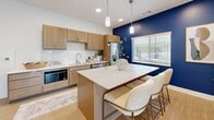 Located in Blair, Nebraska, this single-floor amenity space is thoughtfully designed to serve both functional and recreational needs. The interior is bright and modern, characterized by clean white walls accented with bold color choices that give each area a distinct personality.

The kitchen is a standout feature, showcasing warm natural wood cabinetry paired with crisp white quartz countertops and a classic white subway tile backsplash. A central island with seating offers a casual dining or gathering space, illuminated by pendant lighting overhead. Stainless steel appliances, including a full-size refrigerator and dishwasher, complement the space, while a large window with blinds floods the room with natural light. A deep navy blue accent wall adds a striking visual contrast to the warm wood tones and light flooring.

A welcoming lounge corridor connects the spaces, featuring light wood-look flooring, framed artwork, and a teal accent wall that adds vibrancy to the transitional area. Comfortable seating makes it an inviting place to pause.

The exercise room is well-equipped with durable rubber flooring, a full cable functional trainer, a complete dumbbell rack set, a cycling bike, and a treadmill. Recessed lighting and a window providing natural light create an energizing workout environment. Together, these spaces offer a comprehensive and polished amenity experience.