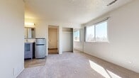 This efficiently designed single-floor unit offers a thoughtful layout across four distinct areas: an entrance, kitchen, bedroom, and bathroom. The bedroom is the largest space in the unit, featuring plush carpeting, a textured ceiling, and a wide sliding mirrored closet that adds depth to the room. A generously sized window fills the space with natural light and offers a pleasant outdoor view of surrounding trees and sky. The galley-style kitchen is well-appointed with white shaker cabinetry, granite-look countertops, a stainless steel sink with modern faucet, and full-size appliances — including a refrigerator and range — all set atop light wood-look flooring. A sliding glass door at the end of the kitchen leads to an outdoor balcony, bringing in additional natural light. The bathroom is clean and functional, featuring a combination tub and shower with a curtain, a toilet, and wood-look flooring with a textured wall finish. The entrance area provides a welcoming transition into the unit with a dedicated entry door and carpeted flooring. Neutral tones throughout create a cohesive and calming atmosphere, making this a practical and comfortable living space.