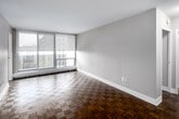 Located on the 15th floor at 255 Glenlake Ave in Toronto's Junction neighbourhood, this unit offers a well-organized single-floor layout with a neutral, understated aesthetic throughout. Rich parquet wood flooring runs through the living areas and bedrooms, adding warmth and character to the space.

The living area is bright and open, featuring floor-to-ceiling windows fitted with roller blinds that provide both natural light and privacy, along with sweeping views of the surrounding cityscape. A baseboard heating system lines the perimeter of the windowed walls. The entry foyer provides ample storage with double closet doors, offering practical organization from the moment you step inside.

The bedroom spaces are comfortably sized, each benefiting from large windows with outdoor views and baseboard heating. One bedroom includes a ceiling fan and roller blind, while another features a corner window arrangement that maximizes natural light and city views.

The kitchen is equipped with light wood cabinetry, white countertops, tile flooring, and a stainless steel refrigerator, offering a clean and modern feel. The bathroom is finished in white tiling with a full soaker tub and shower combination, a vanity with an integrated sink, and a large mirror.