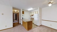 Located at 74 Muirwood Village Dr in Delaware, Ohio, this single-floor residence offers a practical and comfortable layout designed for everyday living. The kitchen serves as a central feature of the space, equipped with a peninsula-style counter that provides additional workspace and casual seating potential. White appliances, including a full-size refrigerator, dishwasher, and range, are complemented by a combination of wood-toned and light-colored cabinetry that offers generous storage. A flush-mount fluorescent light fixture ensures the kitchen is well-lit. The kitchen transitions seamlessly to the carpeted living area, creating an open, connected feel. A hallway extending from the main living space leads to additional rooms, suggesting a well-organized floor plan. The interiors feature neutral tones throughout, with cream-colored walls, light carpet, and warm wood accents contributing to a cohesive and understated aesthetic. Textured ceilings and clean white baseboards add subtle architectural detail. Overall, the space presents a functional and tidy environment well-suited for comfortable, single-level living.