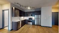 This single-floor unit offers a thoughtfully designed layout that balances modern aesthetics with functional living. The kitchen is a standout feature, showcasing dark espresso cabinetry extending to the ceiling, granite countertops, and a classic herringbone tile backsplash. A full suite of stainless steel appliances — including a refrigerator, range, over-the-range microwave, and dishwasher — provides a polished, cohesive look. Distinctive track lighting with an artistic branching fixture adds a contemporary touch overhead, while light wood-tone flooring flows throughout the space, creating a warm contrast to the dark cabinetry.

The open living area is spacious and bright, with neutral-toned walls and the same warm hardwood-style flooring continuing seamlessly from the kitchen. A set of glass French doors leads to a private balcony, allowing natural light to fill the room and offering an outdoor retreat.

The unit includes two bathrooms finished in a clean, minimalist style. Both feature large-format white tile flooring, dark vanity cabinetry with modern hardware, and white countertops. One bathroom includes a full soaking tub with shower combination, while the other provides a compact, functional layout with a single vanity. The overall ambiance is modern, cohesive, and move-in ready.