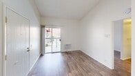 This one-bedroom, one-bathroom unit offers a well-organized single-floor layout designed to maximize functionality within a compact footprint. The living area serves as the heart of the unit, featuring warm wood-style laminate flooring and crisp white walls that create a clean, bright aesthetic throughout. A sliding glass door opens directly onto a private balcony, providing outdoor access and allowing natural light to fill the space. A wall-mounted HVAC unit ensures climate control within the living area.

The bedroom is a comfortable, defined space with its own window fitted with vertical blinds, offering views of the surrounding exterior and admitting additional natural light. Textured ceilings are present throughout the unit, adding subtle depth to the otherwise minimalist interior. A dedicated closet provides practical storage directly accessible from the living areas.

The bathroom features a single-basin vanity with a speckled countertop and a large mirror, maintaining the unit's clean and functional design language. An entrance area provides a clear transition point upon entry. The overall layout, as reflected in the floor plan, flows logically from the entrance through the living space and into the private bedroom and bathroom, making efficient use of every area within the unit.