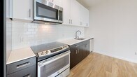 Located at 22 Etruria St in Seattle's Queen Anne neighborhood, this modern one-bedroom, one-bathroom residence offers a thoughtfully designed layout making efficient use of its compact footprint. Light wood plank flooring runs throughout, lending warmth and visual continuity to every room.

The open-concept kitchen and living area serves as the heart of the unit. The kitchen is well-appointed with stainless steel appliances including a slide-in range, built-in microwave, and refrigerator, complemented by dark lower cabinetry, crisp white upper cabinets, white quartz countertops, and a classic subway tile backsplash. The adjacent living area is bright and airy, featuring large floor-to-ceiling windows and a glass door that opens onto a private balcony, allowing ample natural light to fill the space.

The bedroom is a comfortable, quiet retreat with its own window, a ceiling fan, baseboard heating, and access to two closets. The bathroom features a wide dark-cabineted vanity with a vessel sink and a well-lit mirror. An in-unit laundry area adds everyday convenience. The hallway connects all spaces cleanly, with a louvered closet door providing additional storage. This unit offers a clean, modern aesthetic well-suited for comfortable urban living in Seattle.