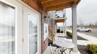 Located at 5927 Avery Wood Ave in Dublin, Ohio, this single-floor residence combines classic architectural character with comfortable outdoor living. The exterior showcases a traditional red brick facade, lending the property a timeless and sturdy appeal that is immediately welcoming.

One of the standout features of this space is the covered patio area, which serves as a seamless transition between the interior and the outdoors. The patio is topped with a natural wood-planked ceiling, adding warmth and a refined aesthetic to the outdoor space. Wall-mounted lantern-style light fixtures flank the entryway, contributing to the unit's classic curb appeal. The patio comfortably accommodates outdoor seating, making it an inviting spot for relaxation or casual dining while overlooking the well-maintained landscaping and open neighborhood surroundings.

Large glass sliding doors connect the covered patio to the interior, allowing for generous natural light and easy indoor-outdoor flow. The building's design incorporates an upper-level balcony visible from the patio, reinforcing the architectural cohesion of the community. The surrounding landscape features neatly arranged greenery and a clean, open setting with views reaching toward the broader Dublin neighborhood. Overall, the property presents a blend of traditional craftsmanship and functional design in a well-established community setting.