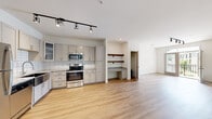 Located at 1000 Sweet Almond Dr in Holly Springs, NC, this well-appointed two-bedroom, two-bathroom residence offers a thoughtfully designed single-level layout with a bright, open feel throughout. The kitchen is outfitted with stainless steel appliances, including a range, microwave, refrigerator, and dishwasher, complemented by gray shaker-style cabinetry, a tile backsplash, and granite-look countertops. Track lighting overhead adds a modern touch. Adjacent to the kitchen is a convenient built-in desk nook with wood shelving, ideal for a home office setup. Light wood-tone flooring flows through the main living areas, creating a clean and cohesive aesthetic. The living area opens to a private balcony, allowing for natural light and outdoor views. Both bedrooms feature plush carpeting and ceiling fans, with the spacious primary bedroom offering its own en-suite bathroom equipped with a walk-in shower, granite countertop vanity, and gray cabinetry. The second bathroom includes a full tub-shower combo with the same consistent finishes. Two closets provide generous storage, including a walk-in closet outfitted with wire shelving systems for organized storage. The overall ambiance is clean, modern, and move-in ready.