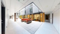 The Divine Court Common Area in Auburn, WA, is a thoughtfully designed shared facility spanning a generous single floor, offering residents a variety of amenity spaces within a modern, multi-story building complex. At its heart is a covered outdoor courtyard with large-format tile flooring, framed by the building's contemporary façade of gray panels and warm wood-toned cladding. The courtyard features wicker lounge seating with bold red cushions, bistro tables, and a ping-pong table, creating a lively recreational hub open to upper-floor views and natural light.

Adjacent interior spaces include a bright lounge area with light hardwood flooring, recessed lighting, colorful artwork, and a mix of seating suited for relaxing or casual gatherings. Large windows connect the lounge directly to the courtyard, maintaining a visual openness throughout. A well-equipped kitchen with white cabinetry and stainless steel appliances supports community events and resident use. A dedicated fitness room features mirrored walls, yoga mats, a weight bench, and cardio equipment, with direct courtyard access. A clean, simply appointed restroom and additional dining and gathering areas complete the amenity suite, all finished in a cohesive, contemporary palette.
