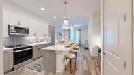 Located at 4040 Valley View Ln in Farmers Branch, TX, this thoughtfully designed one-bedroom, one-bathroom residence offers a modern aesthetic and efficient layout across a single floor. The open-concept kitchen and living area serves as the heart of the home, featuring light wood-style flooring, recessed lighting, and a spacious quartz-topped island with bar seating illuminated by sleek pendant lights. The kitchen is outfitted with two-tone cabinetry — white uppers and wood-grain lowers — a subway tile backsplash, and a full suite of stainless steel appliances including a French door refrigerator, range, and microwave. The living area is bright and welcoming, benefiting from natural light through large windows and a glass door that opens to the outdoors. The bedroom offers a comfortable, carpeted retreat with a ceiling fan and a generous walk-in closet featuring built-in shelving and ample hanging space. The full bathroom is elegantly appointed with a dual-sink vanity in warm wood tones, white quartz countertops, a large framed mirror, and a walk-in glass-enclosed shower with tile surround. Additional spaces include a laundry area and utility room, completing this well-appointed residence.