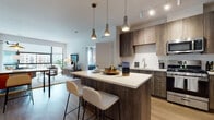This single-floor residence at 200 Market Street in Montvale, New Jersey showcases a contemporary open-concept design with high-end finishes throughout. The kitchen serves as a central hub of the living space, featuring wood-toned cabinetry, a white subway tile backsplash, stainless steel appliances, and a large island with a quartz countertop and built-in seating for two. Pendant lighting and track fixtures illuminate the space effectively. Light wood-style flooring runs throughout, connecting each area cohesively.

The living area is bathed in natural light through expansive floor-to-ceiling windows that frame outdoor views of the surrounding Montvale development. The bedroom continues the bright, airy aesthetic with large windows, light walls, and ample space. A walk-in closet offers generous storage with wire shelving systems. The en-suite bathroom is finished with marble-look tile flooring and walls, a glass-enclosed shower, a dual-sink vanity with wood cabinetry, and a large mirror. A secondary living or flex space features a distinctive blue accent wall, adding a layer of personality to the overall neutral palette.