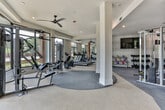 Located at 701–715 Atlanta Student Movement Blvd SW in Atlanta, GA, this single-floor fitness center is designed to accommodate a comprehensive range of workout needs. The space is organized into distinct functional zones that flow seamlessly into one another, creating an open and accessible environment for users of all fitness levels.

The cardio zone features a row of treadmills and additional cardio machines positioned along large floor-to-ceiling windows, allowing abundant natural light to fill the space while providing outdoor views of the surrounding greenery. Ceiling fans overhead contribute to a comfortable workout atmosphere. Teal accent detailing on the tray ceiling adds a modern design touch to this section.

A dedicated strength training area includes a full lineup of selectorized cable and resistance machines, conveniently positioned near the windowed perimeter to maximize natural light. An adjacent free weights section offers a tiered dumbbell rack and a collection of colorful kettlebells, accompanied by a wall-mounted television and a built-in beverage cooler for added convenience.

The flooring transitions between rubberized and carpeted surfaces to suit each zone's function. Textured accent walls, warm wood column details, and strategically placed mirrors throughout enhance both the aesthetic appeal and the sense of spaciousness within the facility.