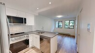 Located at 535–555 Shaw Ave in Coquitlam, BC, this well-designed one-bedroom, one-bathroom unit offers a thoughtfully organized single-floor layout with a clean, contemporary aesthetic. The open-concept kitchen is a standout feature, showcasing white shaker-style cabinetry extending to the ceiling, a classic subway tile backsplash, dark quartz countertops, and a peninsula with an undermount sink. Stainless steel appliances — including a full-size refrigerator, built-in microwave, and dishwasher — complete the modern kitchen ensemble. Light wood-look vinyl flooring flows seamlessly from the kitchen into the living area, which benefits from natural light through black-framed windows with views of greenery outside. The bedroom is a comfortable, bright space with crisp white walls, the same warm flooring, a mirrored sliding-door closet, and baseboard heating. The bathroom is finished in a clean, accessible style with large-format tile flooring, white subway tile surround, a quartz-topped vanity with white cabinetry, a large mirror, and chrome grab bars for added safety. Throughout the unit, white walls, recessed and flush-mount lighting, and consistent flooring choices create a cohesive, modern, and inviting atmosphere.