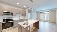 Located at 501 W Washington St in East Peoria, IL, this thoughtfully designed 2-bedroom, 2-bathroom unit offers a clean, modern aesthetic across a single level. The open-concept kitchen is a standout feature, boasting taupe shaker-style cabinetry, a white tile backsplash, quartz countertops, stainless steel appliances, and a spacious center island with pendant lighting — all flowing seamlessly onto light-toned hardwood floors that extend into the living room. The living room is bright and airy, benefiting from natural light and French doors that open onto a private balcony. Both bedrooms are carpeted and feature ceiling fans and windows that invite ample natural light. The primary bedroom is generously sized and is complemented by a well-appointed en-suite bathroom featuring a dual-sink vanity with quartz countertops, grey cabinetry, sleek black-framed mirrors, and a glass-enclosed shower. A dedicated in-unit laundry room with full-size washer and dryer adds everyday convenience. Two closets provide ample storage. The overall ambiance is bright, clean, and contemporary, making this a well-equipped and functional living space.