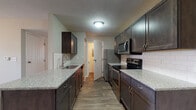 Located at 630 Watkins Glen Blvd in Marysville, Ohio, this single-floor residence offers a well-appointed layout designed for comfortable everyday living. The galley-style kitchen is a standout feature, showcasing rich dark espresso cabinetry with brushed nickel hardware, light granite countertops, a classic white subway tile backsplash, and wood-look flooring. Stainless steel appliances — including a refrigerator, electric range, microwave, and dishwasher — complete the functional and stylish cooking space. The kitchen opens toward the living area, which features plush carpeting, a ceiling fan with light fixture, and a window that invites natural light into the room. The bedrooms are carpeted and finished with neutral-toned walls, offering a calm and versatile environment. The full bathroom includes a tub/shower combination, wood-look flooring, a granite-topped vanity, and clean white finishes throughout. A dedicated laundry room provides added convenience with space for a full-size washer and overhead shelving, along with an accessible electrical panel. The textured ceilings are consistent throughout the home, lending a classic character to each room.