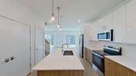 This two-story home in Rowlett, TX offers 1,200 square feet of thoughtfully designed living space across two floors, featuring 3 bedrooms and 3 bathrooms. The 680 sq ft main floor opens into a bright, modern kitchen and living area with light hardwood-style flooring and recessed lighting. The kitchen is a standout, boasting a large center island with a white quartz countertop and built-in sink, two-tone cabinetry combining white upper cabinets with warm wood lower cabinets, stainless steel appliances, and elegant glass pendant lights. A large sliding glass door floods the living area with natural light and provides views of the backyard. The upper floor spans 520 sq ft and hosts all three bedrooms, including a 190 sq ft primary bedroom with plush carpeting, ceiling fan, and multiple windows. Secondary bedrooms also feature carpet flooring, ceiling fans, and windows offering neighborhood views. The three bathrooms are finished with modern tile, wood-tone vanities, and white quartz countertops — two include tub-shower combinations, while one features a glass-enclosed walk-in shower.